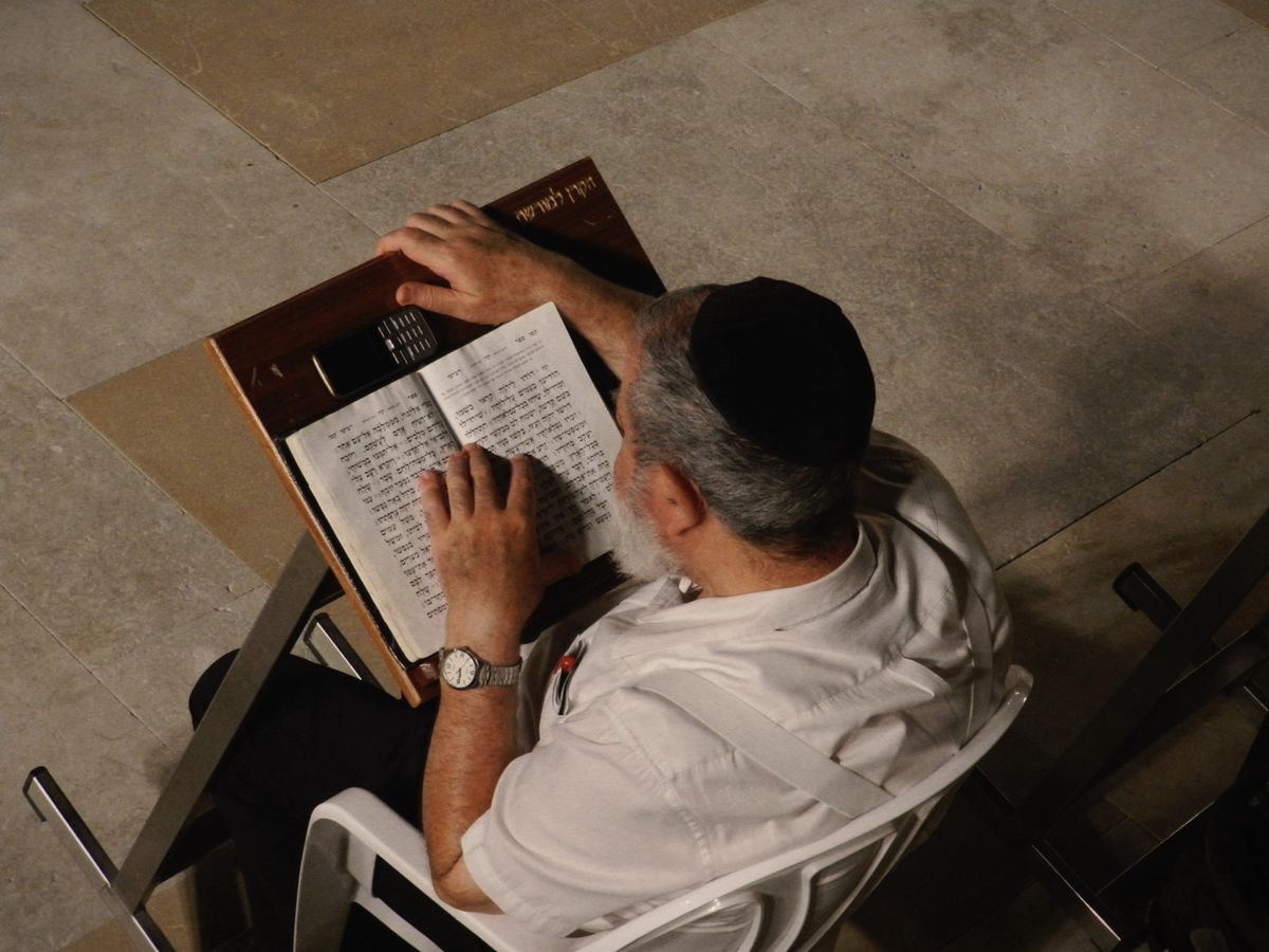 A man in a kippah reading from a siddur at a wooden stand